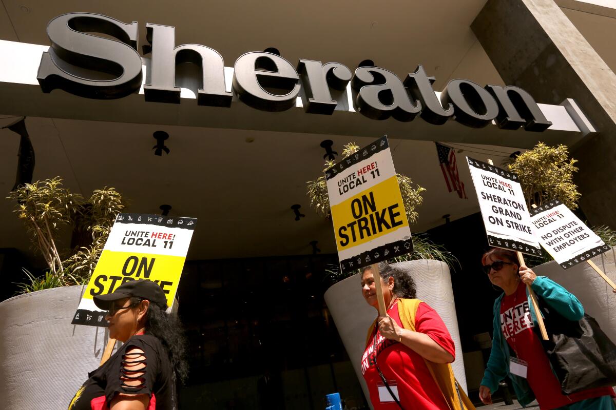 Workers holding picket signs march in front of a Sheraton hotel