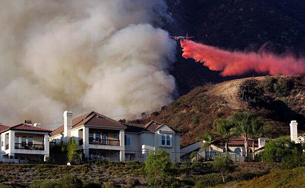 A plane drops fire retardant on a burning hillside above homes in Altadena. The Station fire has consumed more than 21,000 acres, propelled by temperatures that eclipsed 100 degrees and single-digit humidity.