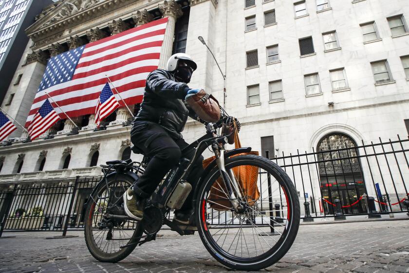 FILE - A delivery worker rides his electric bicycle past the New York Stock Exchange, March 16, 2020, in New York. The city built over 60 miles (100 km) of protected bike lanes from 2019 to 2022, usually connecting them to protected intersections, and a larger number of regular bike lanes. (AP Photo/John Minchillo, File)