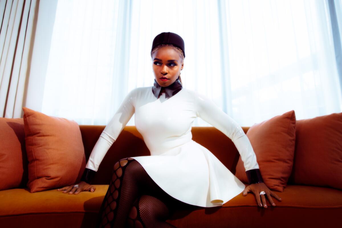 A Black woman in a white dress sits on a sofa with her hands spread out at her sides