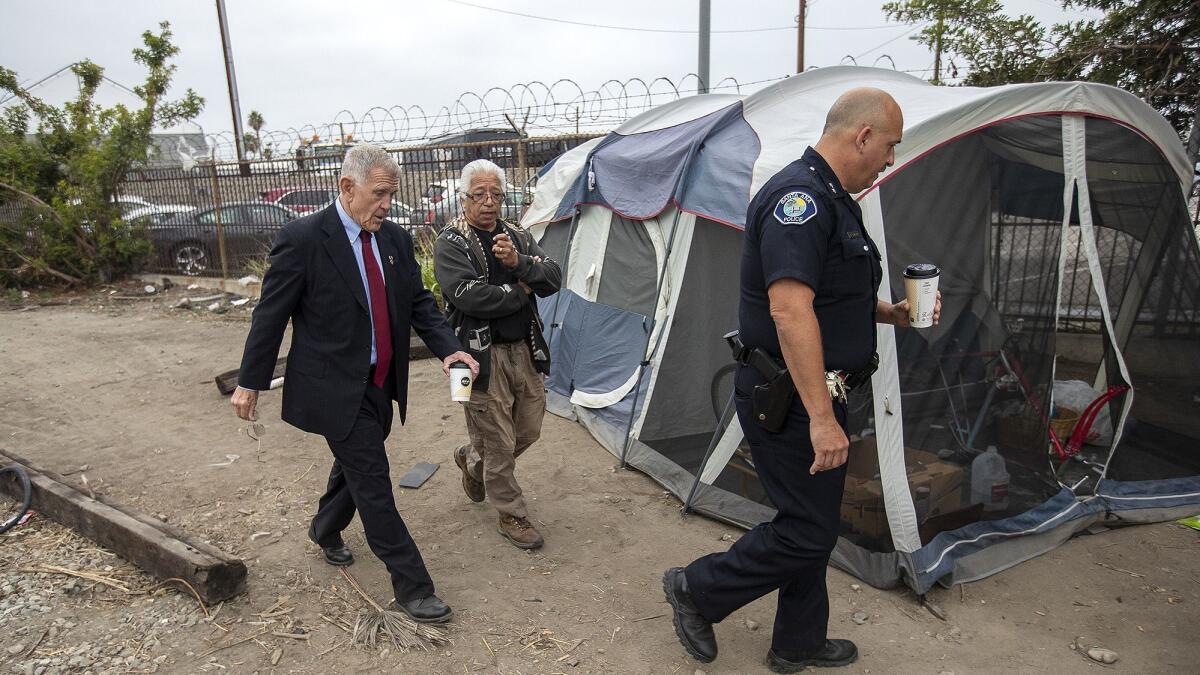 U.S. District Judge David Carter, left, Lou Noble, center, a homeless activist, and Acting Deputy Chief Ken Gominsky of the Santa Ana Police Department walk past a tent along railroad tracks near Goetz Avenue and Main Street in Santa Ana on Tuesday, June 5.