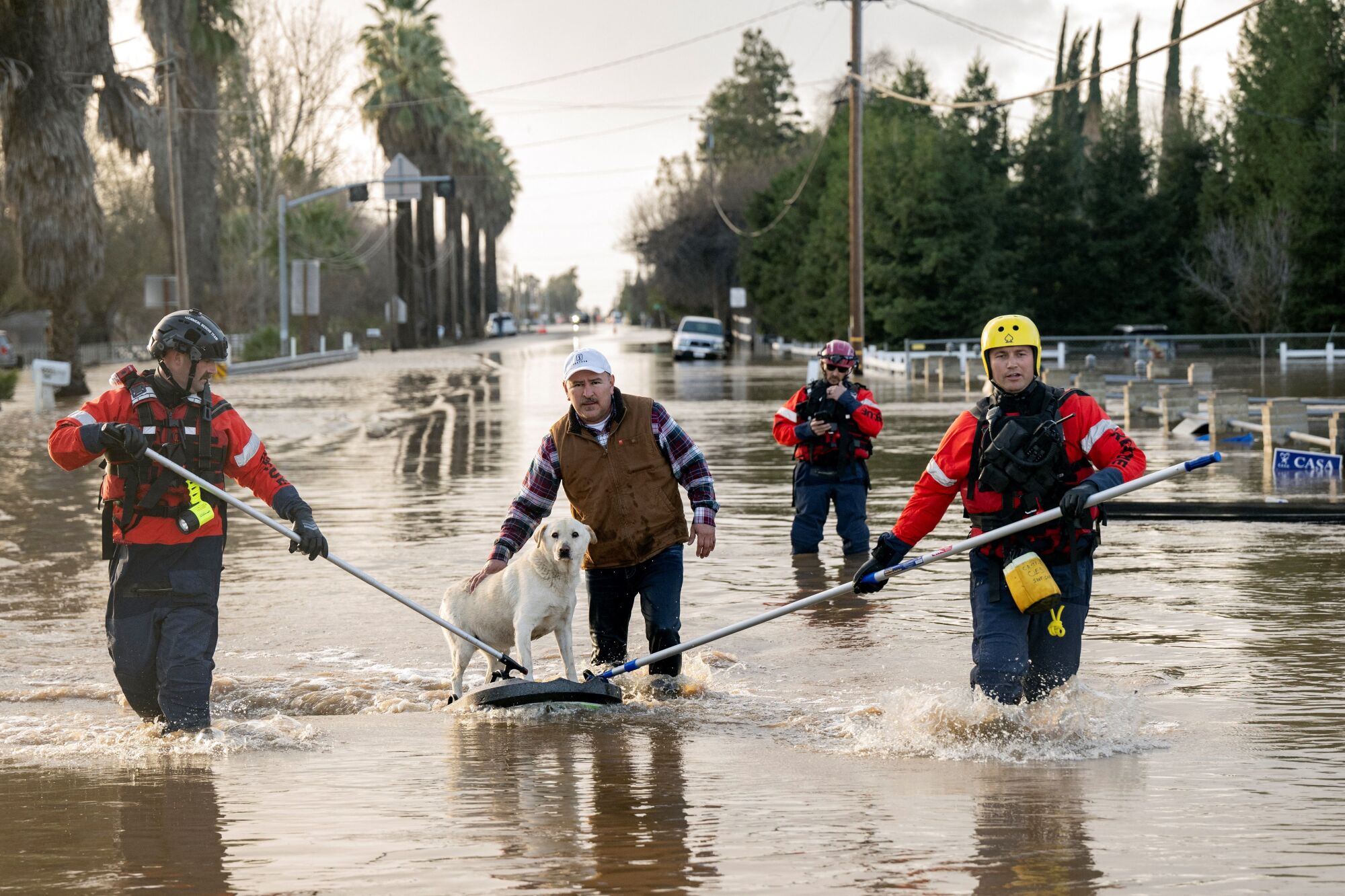 Firefighters help a man rescue his dog from his flooded home .