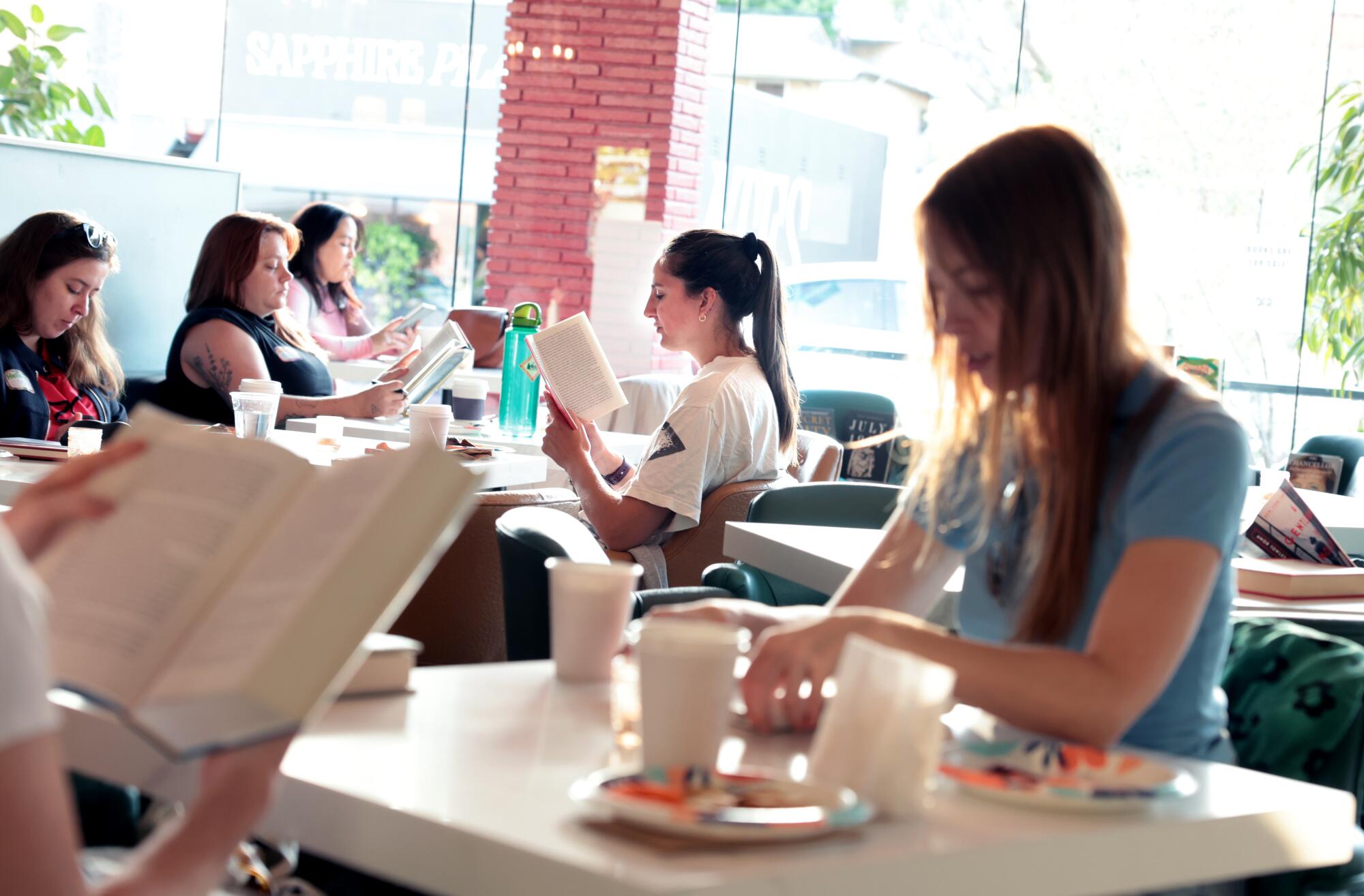 Readers sit at tables in a coffee shop.