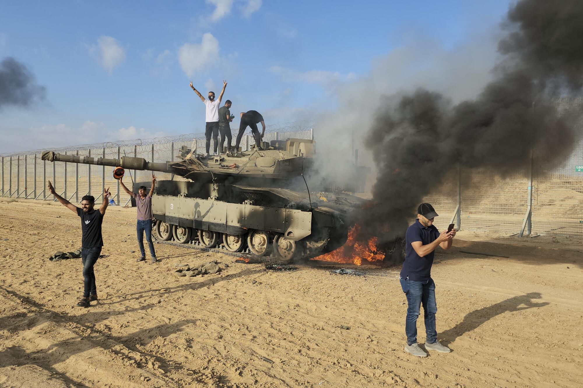 Palestinians celebrating over a destroyed Israeli tank at the Gaza Strip fence