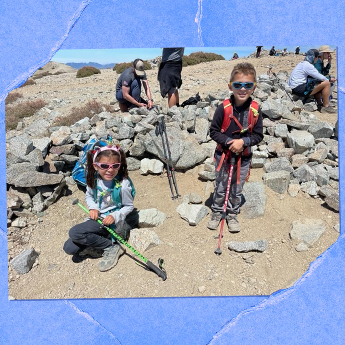 Photo of two children with hiking poles on top of a mountain.