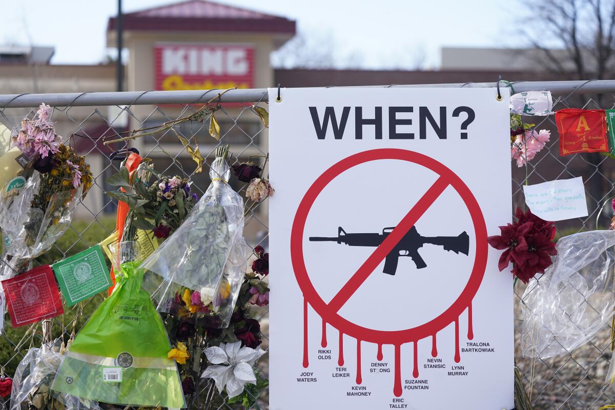Flowers, flags and a sign with a line through an assault rifle hang from the fence outside King Soopers.