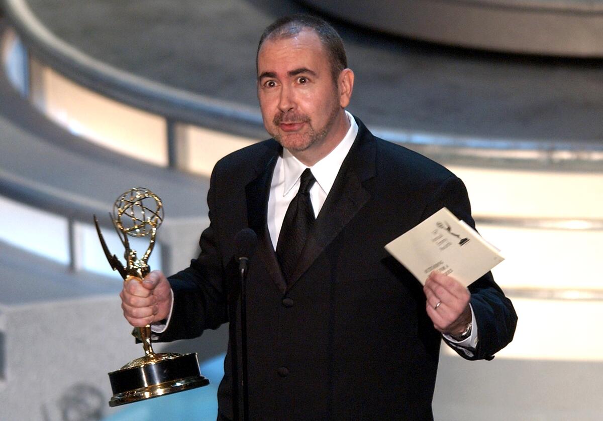 Terence Winter holds an Emmy in one hand and a winner's envelope in the other on stage.