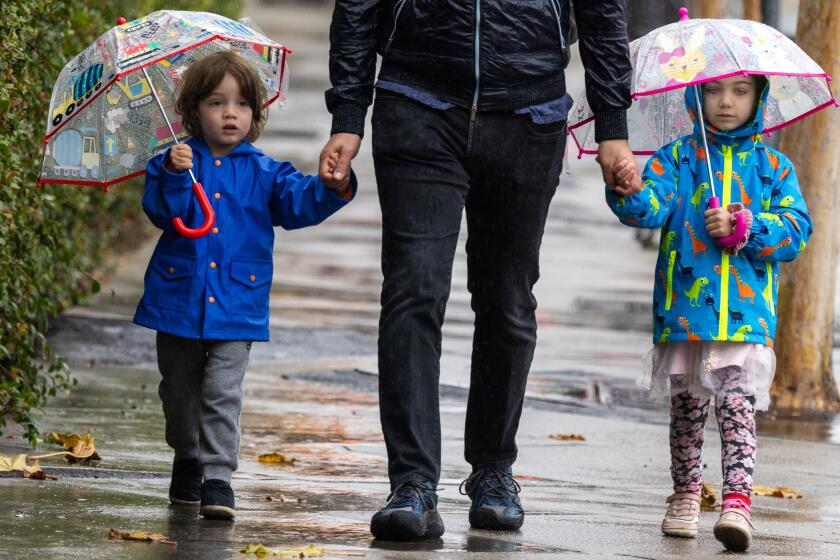 Los Angeles, CA - January 20, 2024: Nerses Sanossian, (CQ) middle, walks her children David, age 3, left, and Amelia, age 5, in the light rain in Pasadena, CA, on Saturday morning January 20, 2024. Nerses says his children love trains. They are walking to the train station to enjoy the Metro ride. (Francine Orr/ Los Angeles Times)