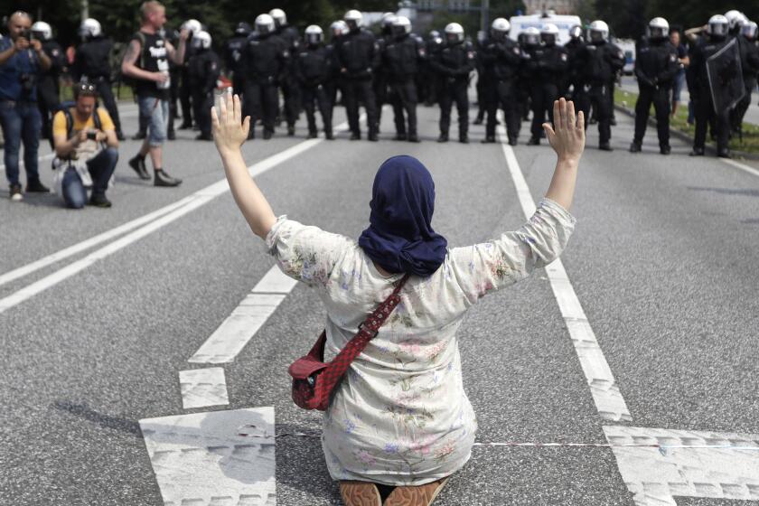 A woman raises her arms as she kneels on a road in front of police officers on the first day of the G-20 summit in Hamburg Germany on July 7, 2017.