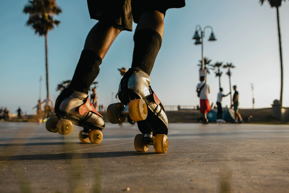 An animated photo gif of roller skates moving up close. Other skaters and a palm tree are in the background.
