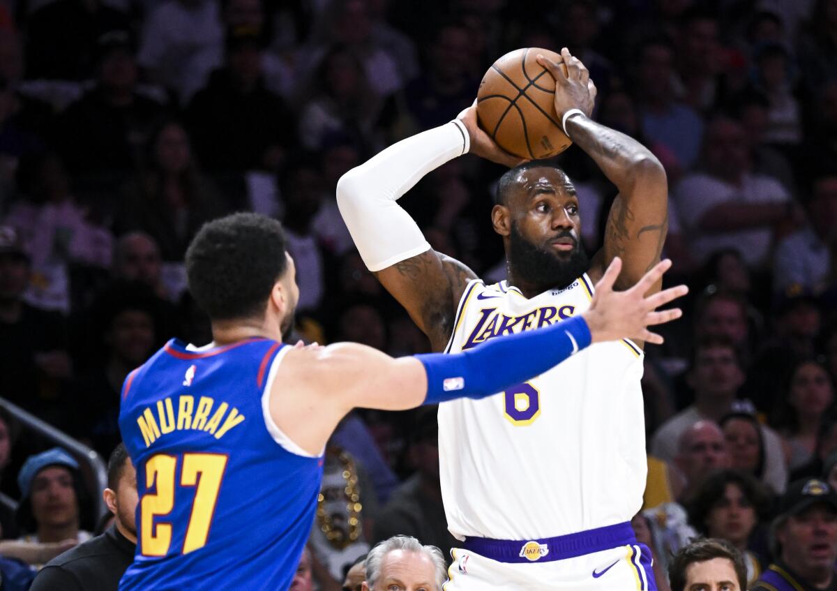 Lakers forward LeBron James, right, holds the ball overhead as he looks to pass while defended by Nuggets guard Jamal Murray.