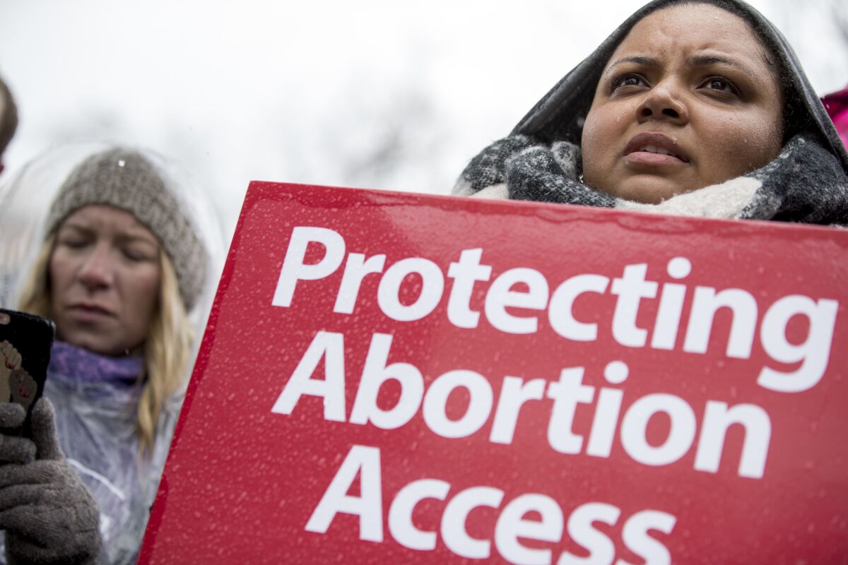 A woman holds a sign that reads "Protecting Abortion Access" 