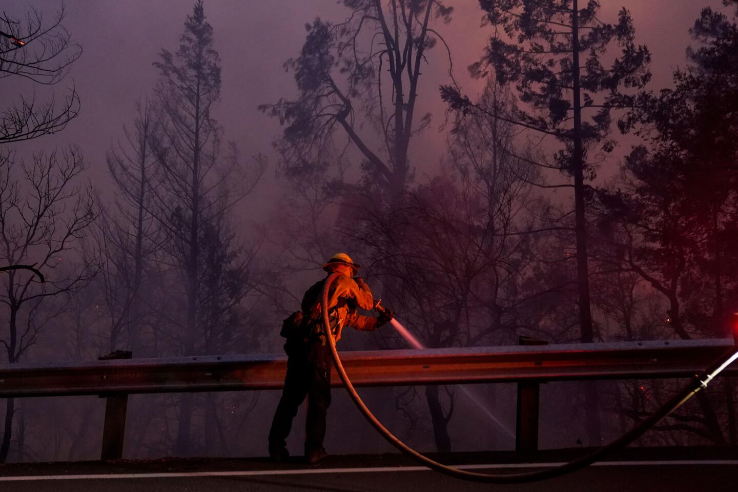 A firefighter sprays water amid thick smoke.
