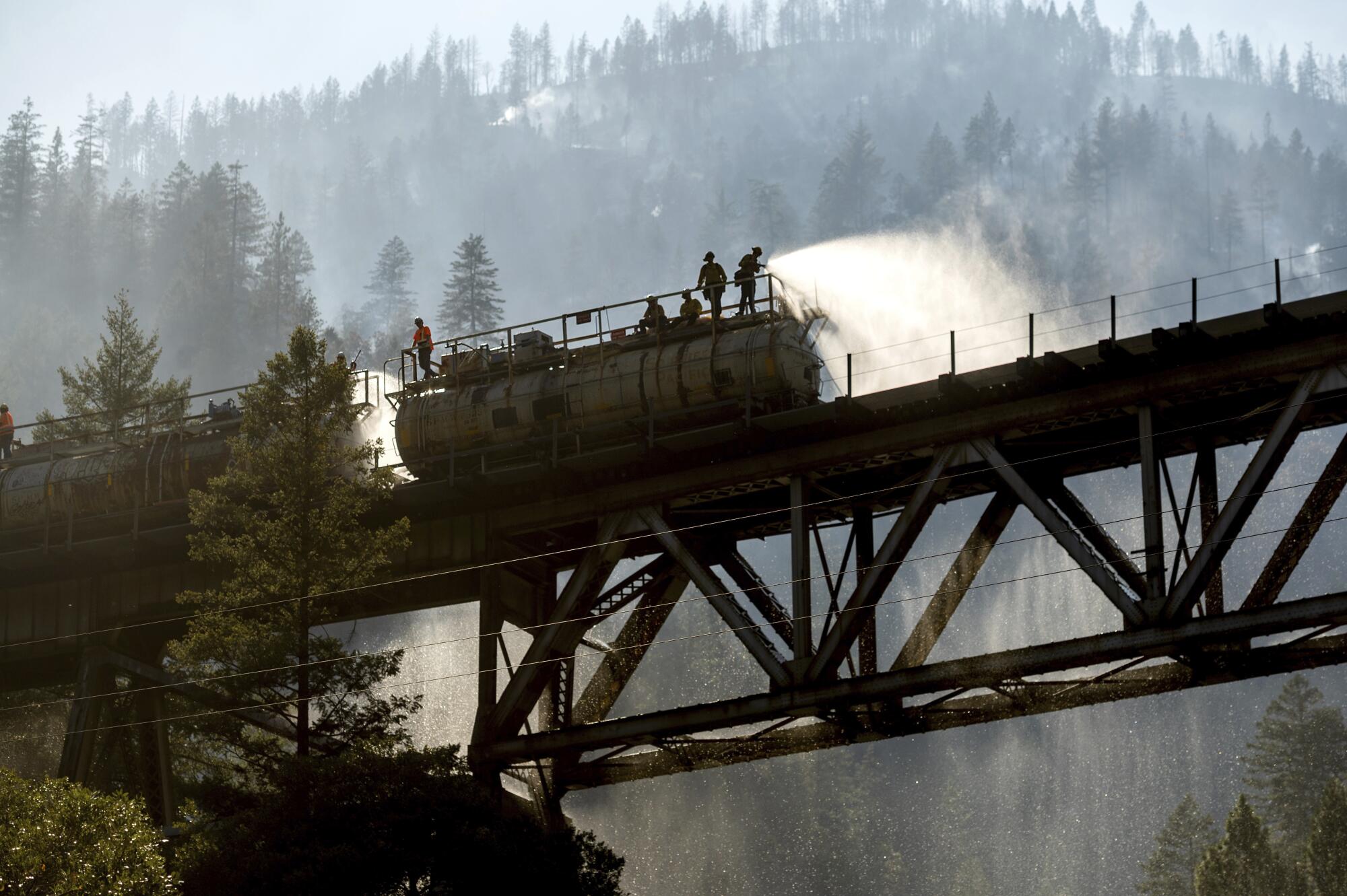Firefighters spray water from Union Pacific Railroad's fire train while battling the Dixie Fire in Plumas National Forest.
