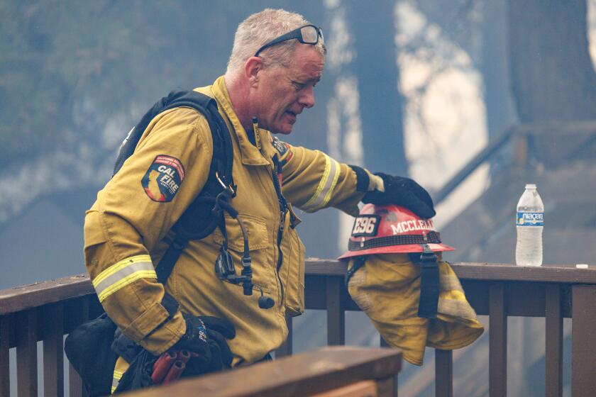 RUNNING SPRINGS, CA - SEPTEMBER 10, 2024: A Cal Fire firefighter takes a break after battling the Line fire in heavy toxic smoke as a home was engulfed in flames on a tree lined neighborhood on September 10, 2024 in Running Springs, California. (Gina Ferazzi / Los Angeles Times)