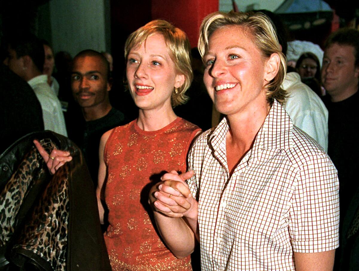 Two women with short blond hair hold hands and smile