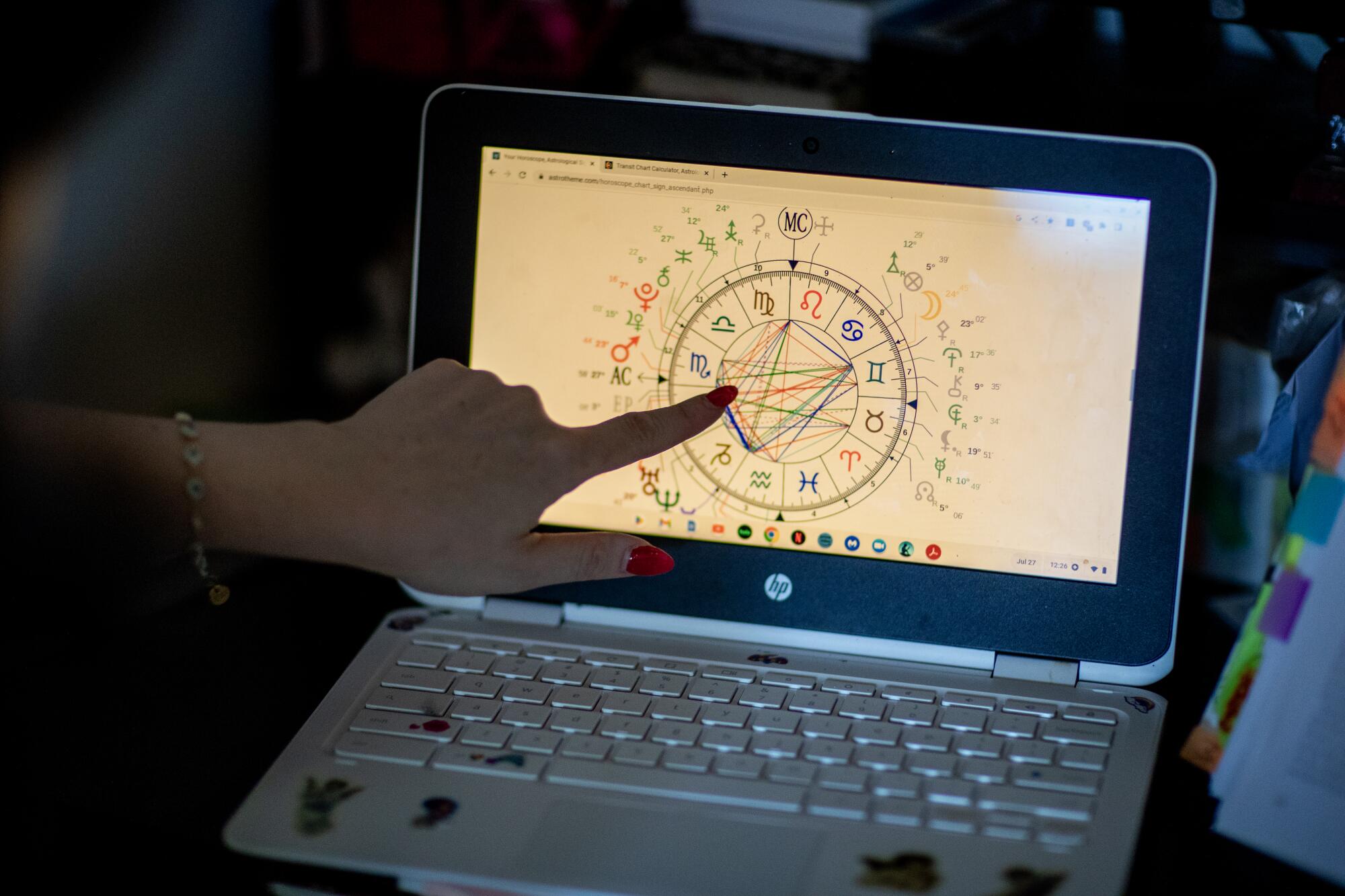 A hand points at an astrological chart on a computer laptop screen.