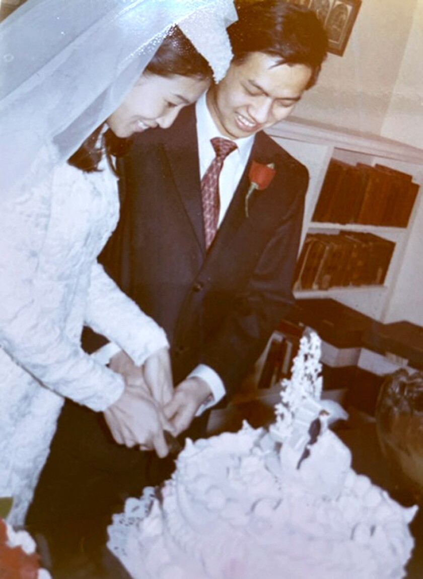 A bride, left, and groom, right, share a knife in cutting a wedding cake