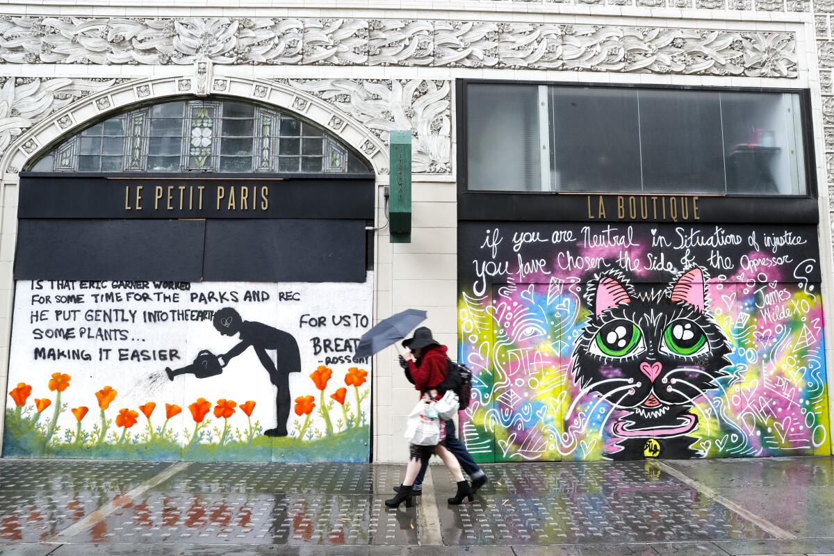 A couple share an umbrella while walking along Spring Street past murals.