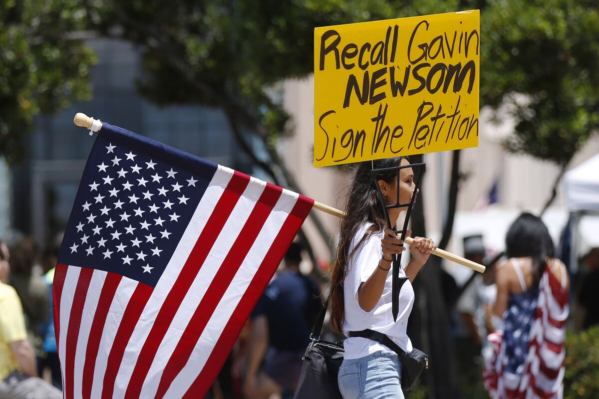 A woman holds up a U.S. flag and a sign pushing to recall California Gov. Gavin Newsom.