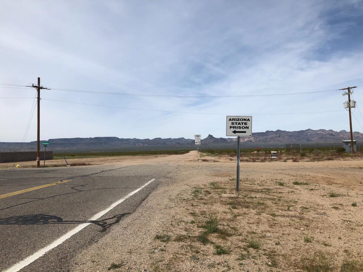 A white sign with a black arrow stands alongside a paved two-lane road cutting through powerlines and desert