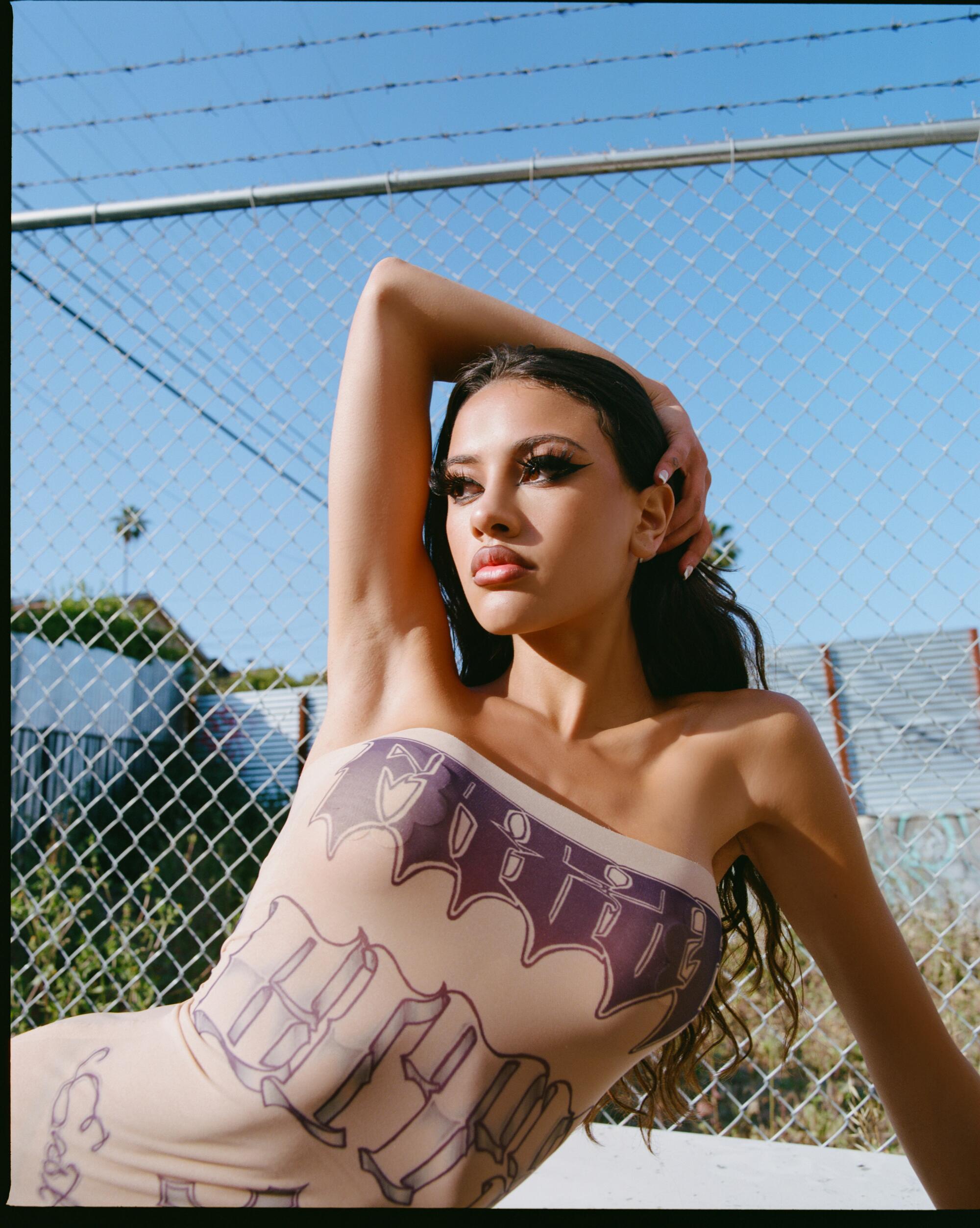 A model is photographed in front of a chain link fence in a dress that resembles tattoos.
