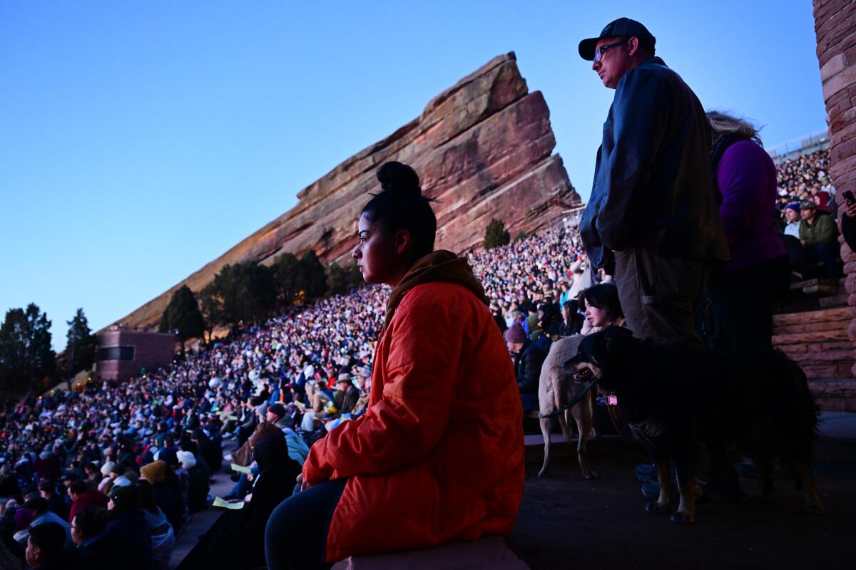 A concertgoer in a red jacket sits at the edge of an amphitheater packed with other attendees