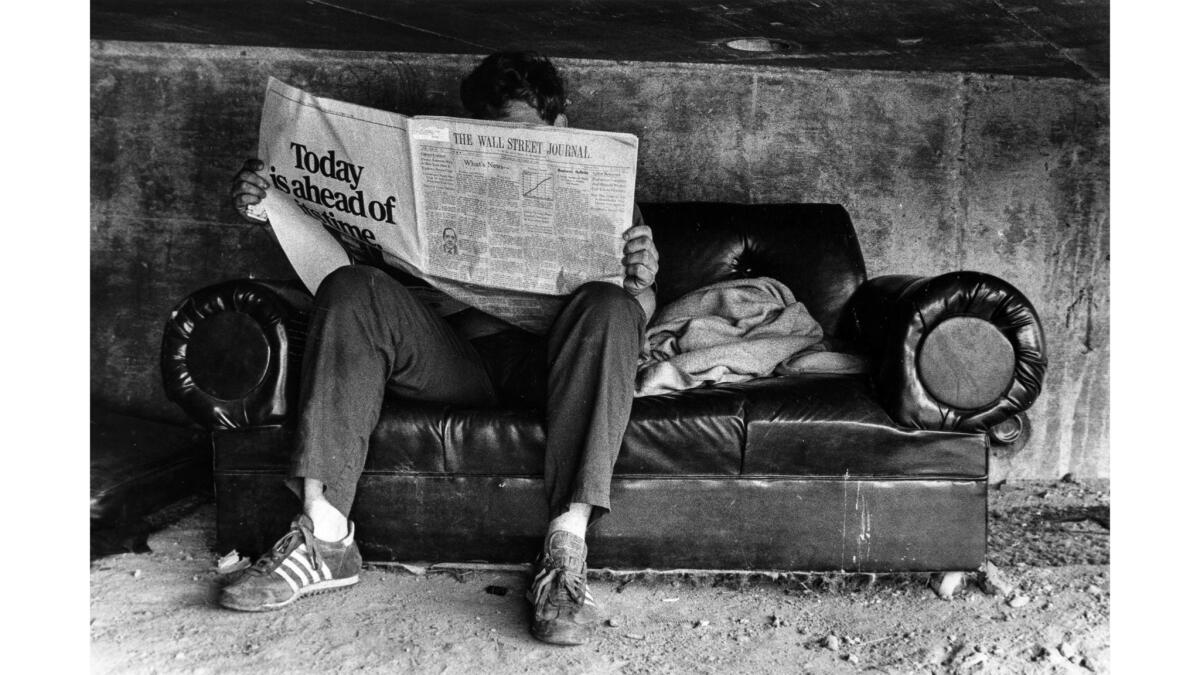 Nov. 8, 1982: A freeway underpass resident sits on a loveseat reading the Wall Street Journal. He and fellow residents, living under Hollywood Boulevard overpass over Hollywood Freeway, carried the loveseat to the site.