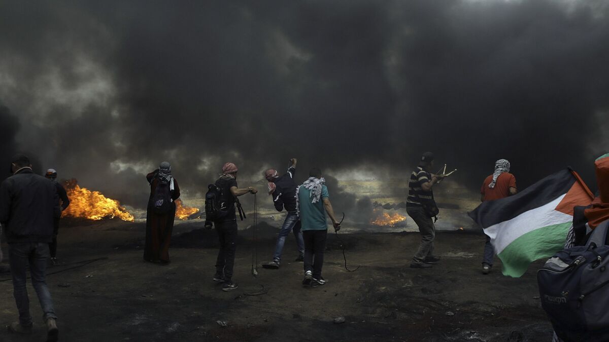 Palestinian protesters in the Gaza Strip hurl stones at Israeli soldiers near the fence amid smoke from burning tires at a May 4, 2018, border demonstration.