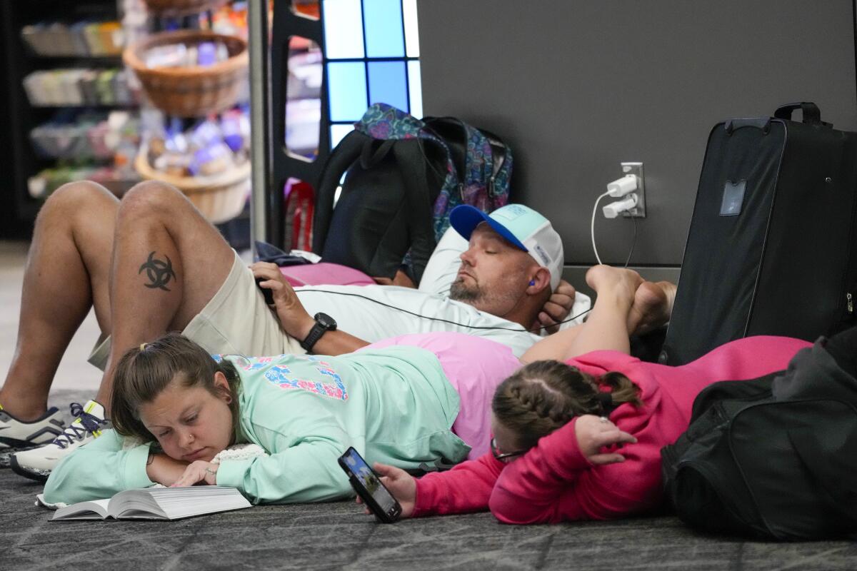 Travelers sit and read on an airport floor.