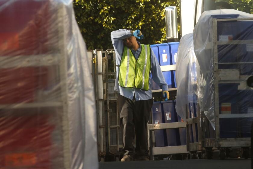 LOS ANGELES, CA - MARCH 25, 2020 - A worker wipes his brow while being surrounded by containers filled with biohazardous waste at Stericycle w in Vernon on March 25, 2020. The company may be dealing with logistical challenges facing medical waste treatment companies during the pandemic. Stericycle, in Vernon, is one of the largest medical waste treatment centers in Southern California. (Genaro Molina / Los Angeles Times)