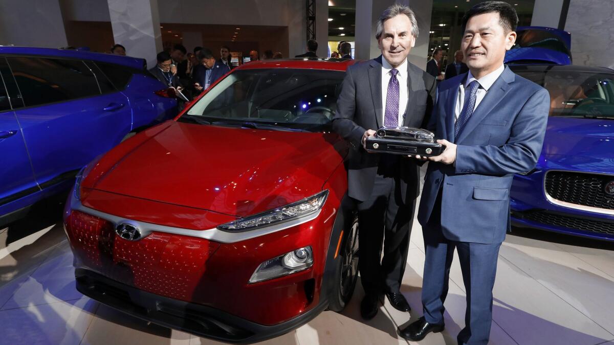 Hyundai Motor North America executives Brian Smith, left, and William Lee hold the North American utility vehicle of the year trophy next to the winning model: the Hyundai Kona.
