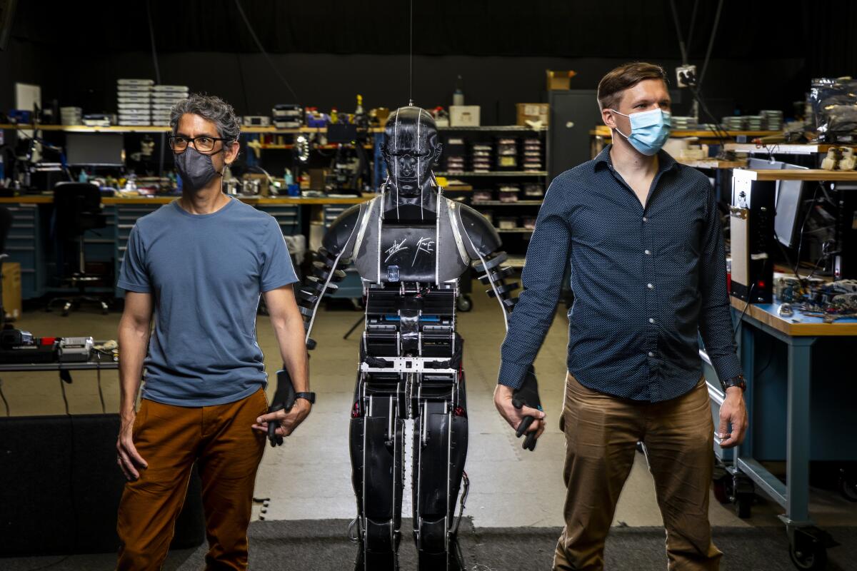 Two men stand while flanking a robot.