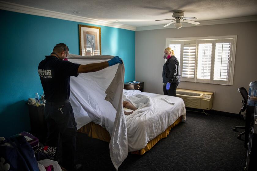 WEST COVINA, CA - OCTOBER 13: Kristina McGuire, an investigator with the Los Angeles County Dept. of Medical Examiner-Coroner, right and Jerry Meza, forensic attendant, prepare to wrap and transport the lifeless body of Judy Bounthong, 58, an ob-gyn tech at Emanate Queen of the Valley Hospital, in her room at the Days Inn by Wyndham, in West Covina, CA, on Tuesday, Oct. 13, 2020. Bounthong died of coronavirus complications, near the end of her isolation period, she wasn't discovered for several days. (Jay L. Clendenin / Los Angeles Times)
