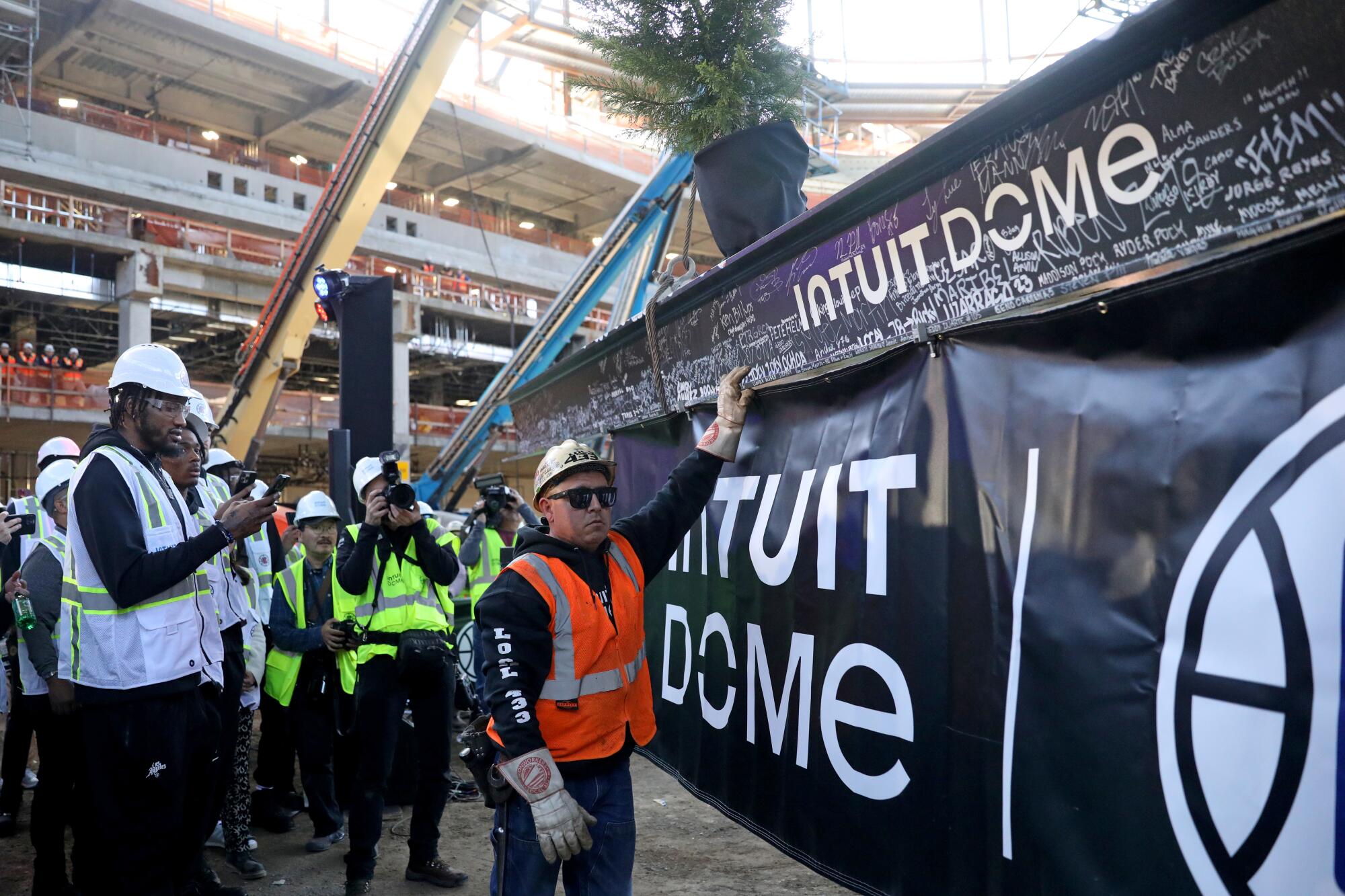 Construction workers prepare to raise a steel beam into place atop the roof of the Intuit Dome.