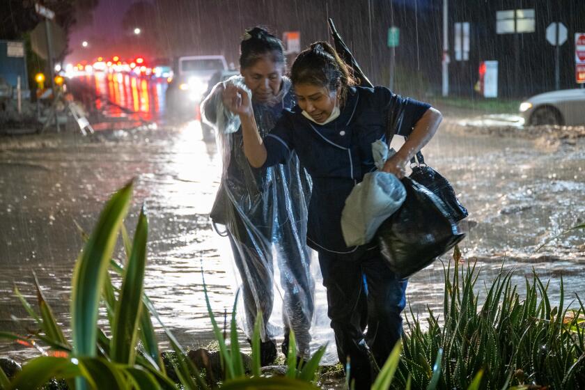 MONTECITO, CA - JAN. 9, 2022: Rosa Gallardo, left, and Connie Duarte cross a flooded street in Montecito after getting off work at their hotel job. (Michael Owen Baker / For The Times)