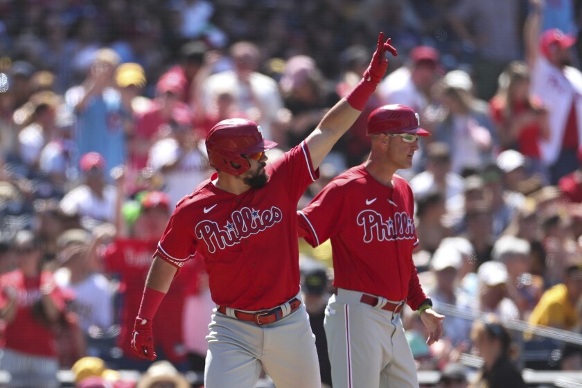 Philadelphia Phillies' Kyle Schwarber, left, gestures towards the outfield after hitting a three run home run against San Diego Padres' Nabil Crismatt as third base coach Dusty Wathan, background, looks on in the seventh inning of a baseball game Sunday, June 26, 2022, in San Diego. (AP Photo/Derrick Tuskan)
