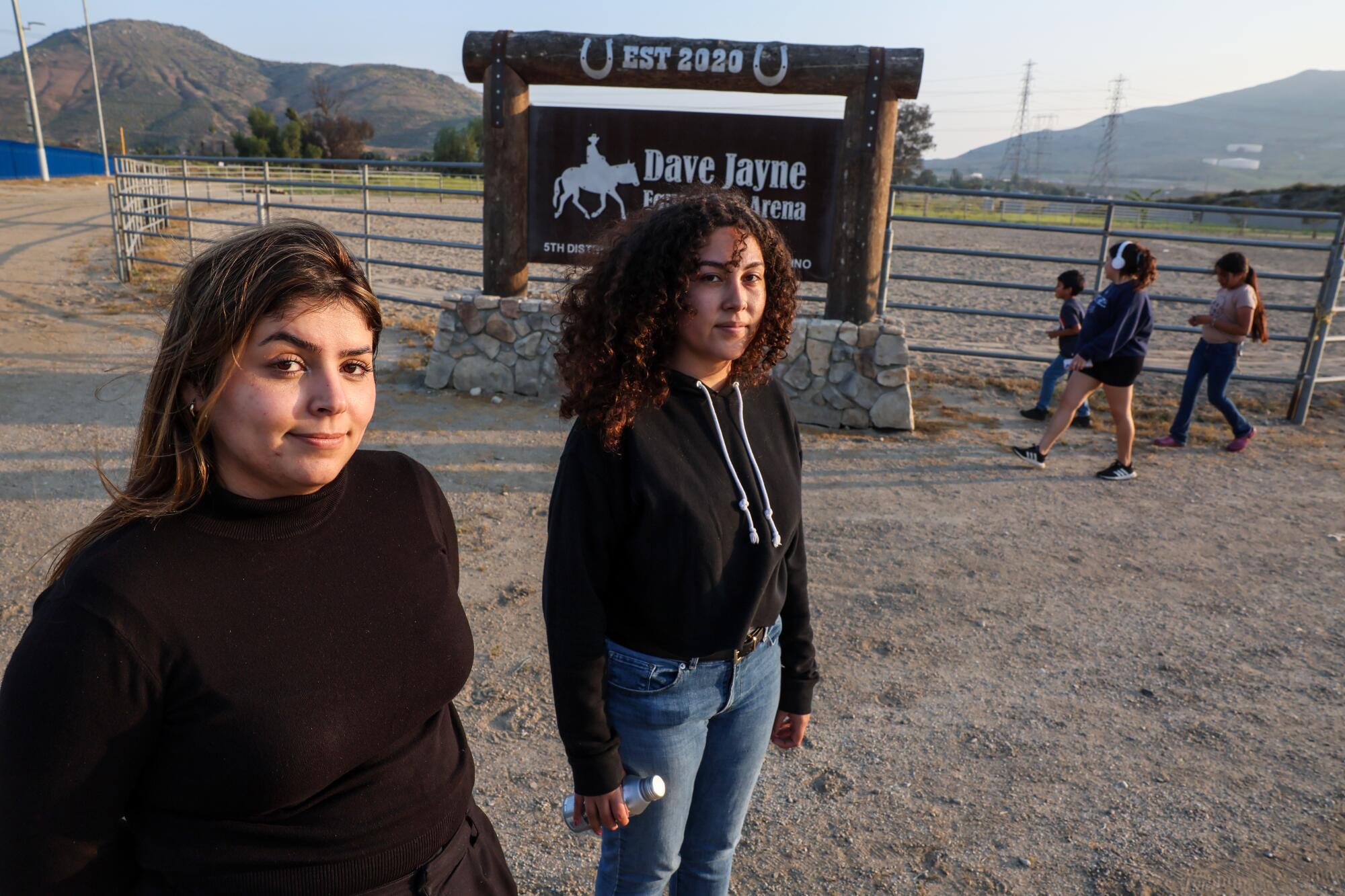 Two young women pose outside a horse corral. 