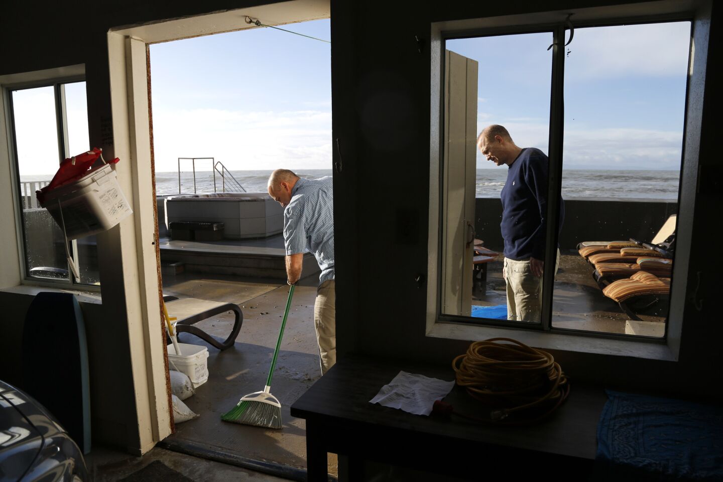 Carlos Pereira, left, tries to clean up an oceanfront deck that was pummeled through the night by big waves.