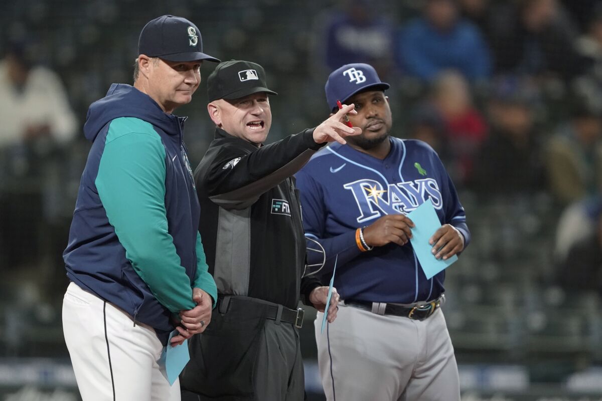 Home plate umpire Mike Muchlinski, center, talks with Seattle Mariners manager Scott Servais, left, and Tampa Bay Rays third base coach Rodney Linares, right, before a baseball game, Thursday, May 5, 2022, in Seattle. (AP Photo/Ted S. Warren)