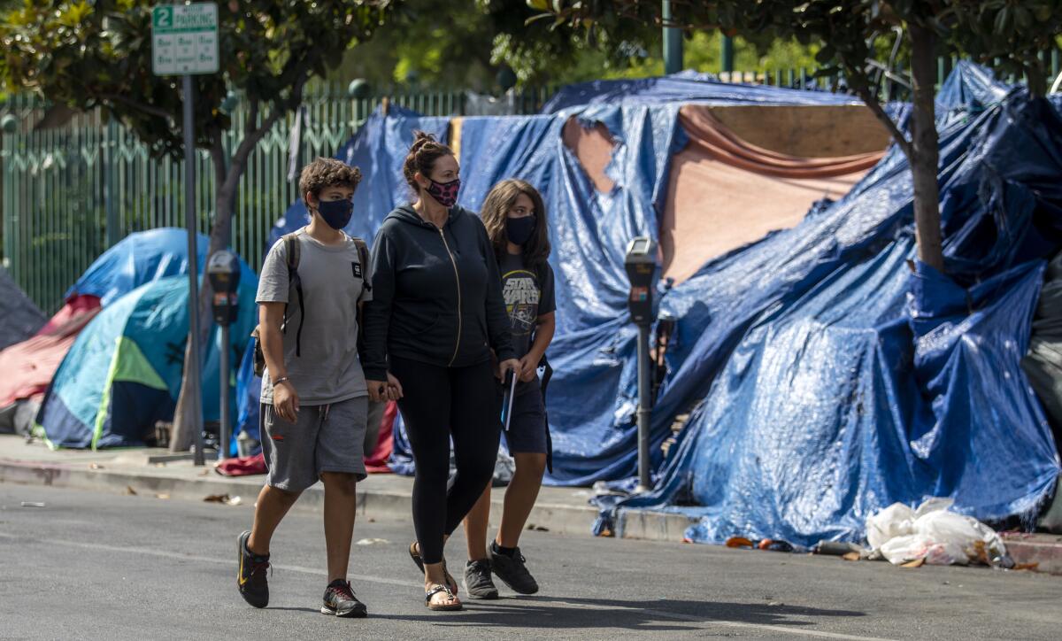 A woman walks with two school-age youths past a homeless encampment in Hollywood