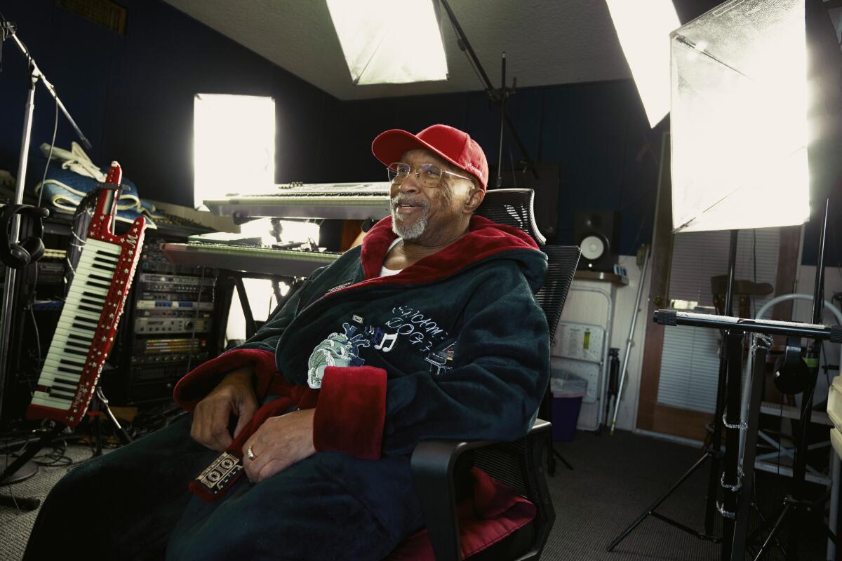 Old black man in red hat and glasses sitting in a robe in his home studio