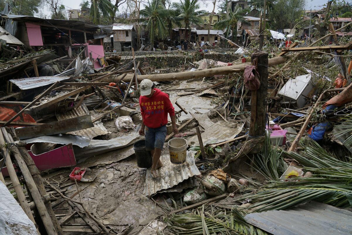 A man carries pails beside damaged homes due to Typhoon Rai in Talisay, Cebu province, central Philippines on Friday, Dec. 17, 2021. A strong typhoon engulfed villages in floods that trapped residents on roofs, toppled trees and knocked out power in southern and central island provinces, where more than 300,000 villagers had fled to safety before the onslaught, officials said. (AP Photo/Jay Labra)