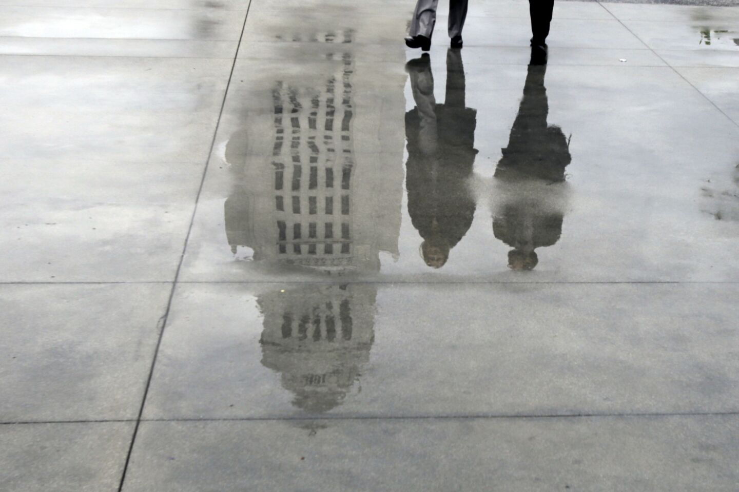 Los Angeles City Hall is reflected in drizzle collected on a walkway at Grand Park in downtown Los Angeles on Tuesday morning.