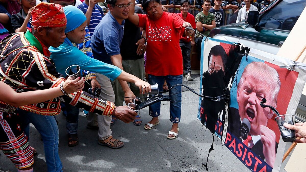 Protesters deface portraits of Presidents Trump and Rodrigo Duterte during a rally near the U.S. Embassy on Friday in Manila.