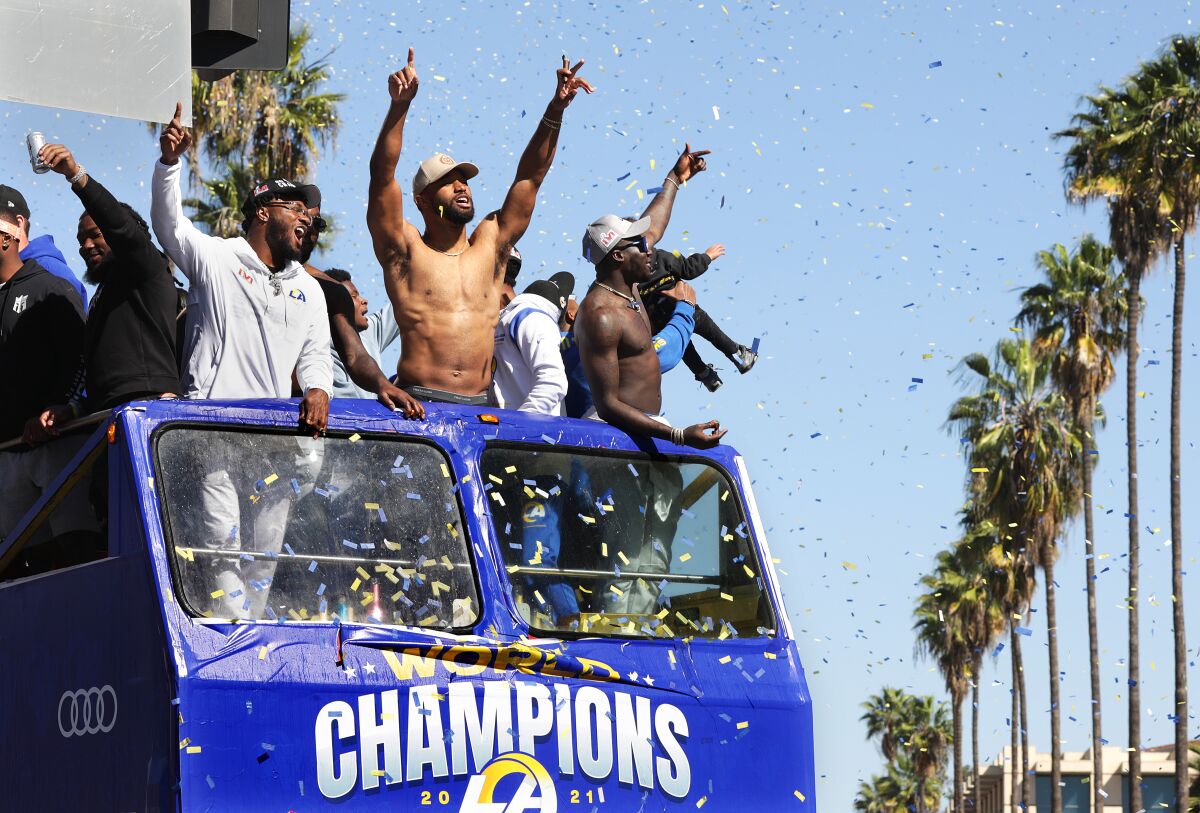Football players riding in a parade raise their arms and shout.