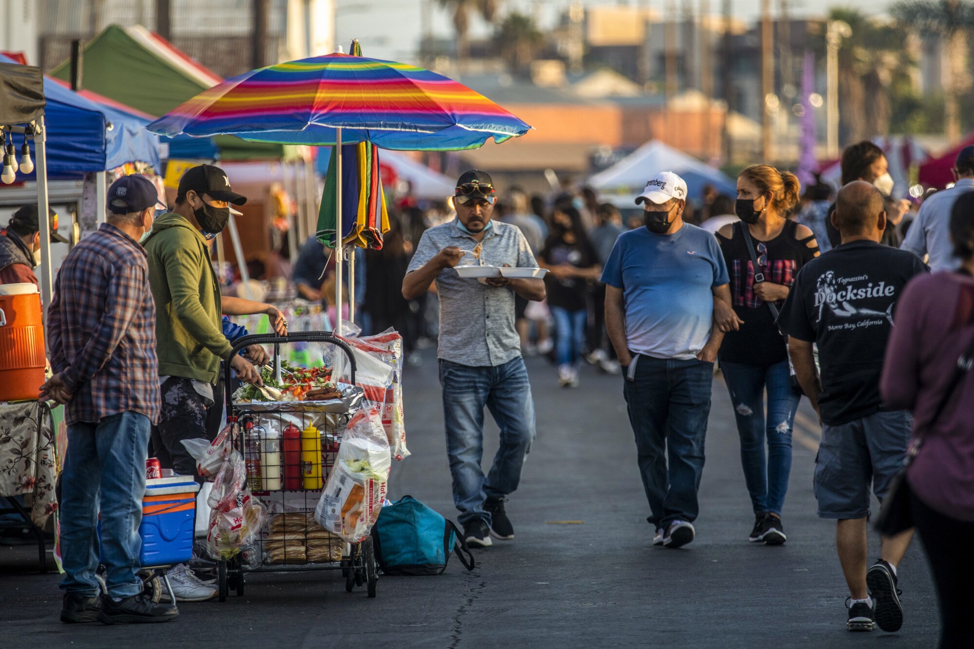 A group of people walk by vendors at a street food market.