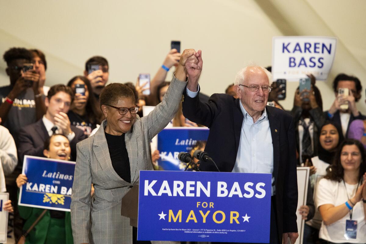 Amid a crowd, a man and a woman raise joined hands behind a sign that says "Karen Bass for mayor."