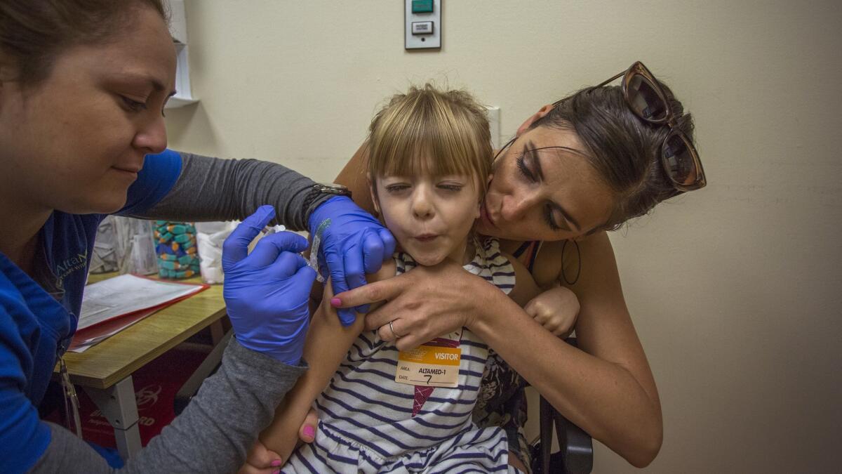 Raven Summers, held by her mother Jessica Summers, holds her breath as she receives a vaccination from medical technician Lilliana Lopez at Children's Hospital Los Angeles in 2017.