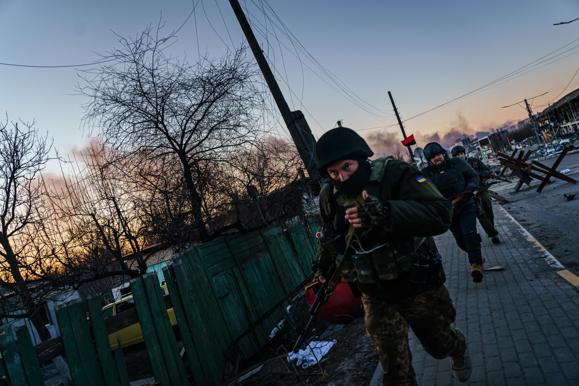 Ukrainian soldiers run cautiously along a sidewalk.
